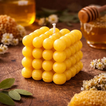 Honeycomb-shaped beeswax candle with raw honey, honeycomb, and chamomile flowers on rustic wood