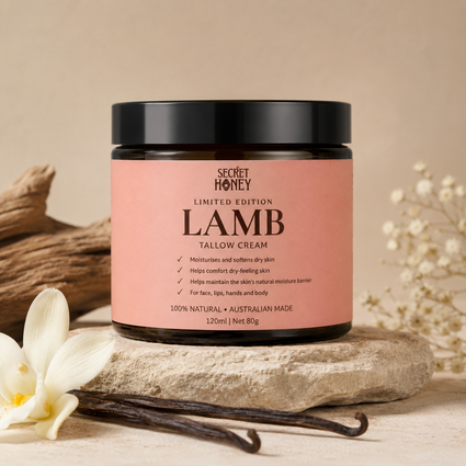 A jar of Secret Honey Limited Edition Lamb Tallow Cream sits on a stone slab with vanilla beans and dried flowers in a warm, neutral setting.